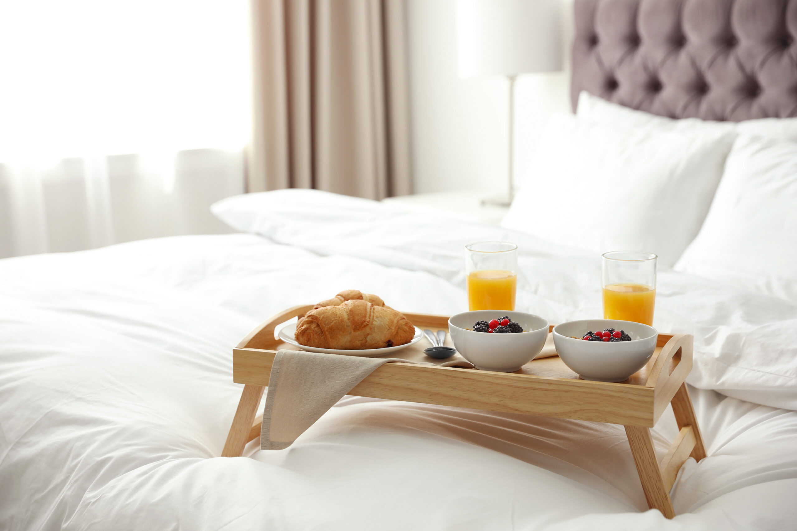 Tray with tasty breakfast on bed in light room